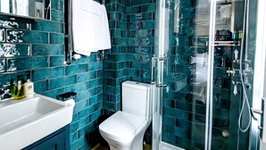 A bathroom with teal mosaic tiles, a white toilet, a sink with toiletries, and a glass-enclosed shower. - 82A Dalston Lane Terrace (London)