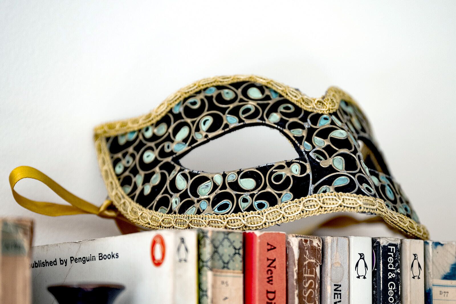 A decorative mask with intricate patterns and a gold trim, placed on a stack of books.