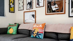 A living room with a grey sofa, various framed artworks on the wall, and colorful throw pillows. - 82A Dalston Lane Terrace (London)
