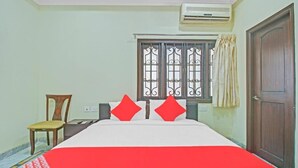 A hotel room with a bed, a chair, a window with bars, and an air conditioning unit.