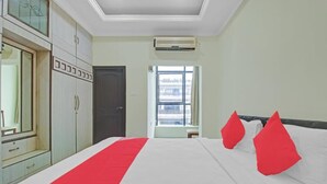 A hotel room with a large bed, a wardrobe, a mirror, a window with a view, and an air conditioning unit.