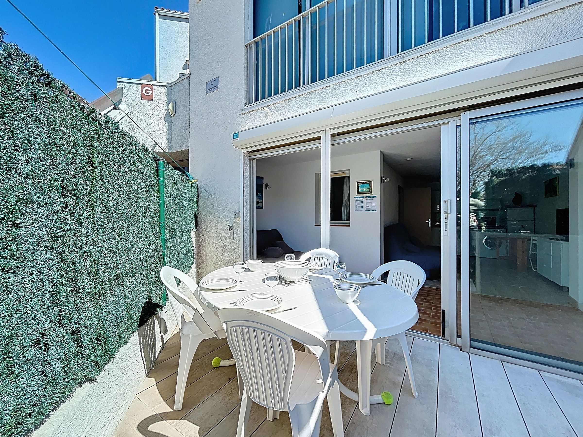 A patio with a table set for dining, surrounded by white chairs, and a glass door leading to an interior space.