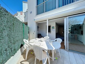 A patio with a table set for dining, surrounded by white chairs, and a glass door leading to an interior space.