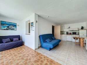 A living room with a blue sofa and a purple sofa, a kitchen with a microwave and a refrigerator, and a tiled floor. - Seafront apartment with terrace and pool (Saint-Cyprien)