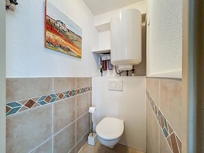 A bathroom with a toilet, a water heater, and a tiled backsplash. - Seafront apartment with terrace and pool (Saint-Cyprien)