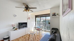 Una sala de estar moderna con ventilador de techo, televisor, sofá, una mesita y un balcón con vistas.
