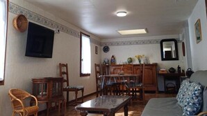 Un salon avec une table en bois, des chaises, un canapé, un téléviseur fixé au mur et un ventilateur de plafond.