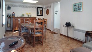 Un coin repas avec une table ronde et des chaises, une horloge au mur et un radiateur sur le côté droit.