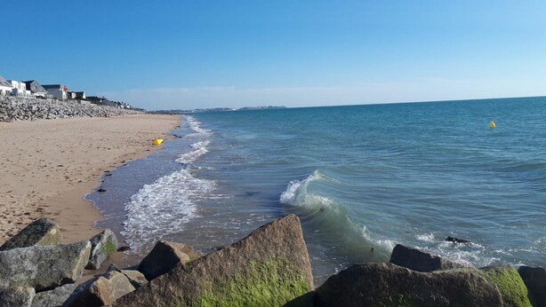Une plage bordée d’une côte rocheuse, un ciel bleu dégagé et une mer calme.