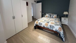 A bedroom with a bed, a nightstand, a wardrobe, and a door leading to another room. - Single-storey house with air conditioning, 3 bedrooms, near the beach (Valras-Plage)