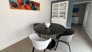 A dining area with a round black table, two white chairs, and a white bowl. A colorful abstract painting is on the wall. - Single-storey house with air conditioning, 3 bedrooms, near the beach (Valras-Plage)