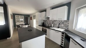 A modern kitchen with white cabinets, a black countertop, and patterned backsplash. - Single-storey house with air conditioning, 3 bedrooms, near the beach (Valras-Plage)