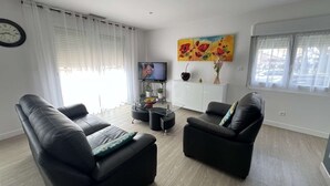 A modern living room with two black leather sofas, a coffee table, a TV, and a painting on the wall. - Single-storey house with air conditioning, 3 bedrooms, near the beach (Valras-Plage)