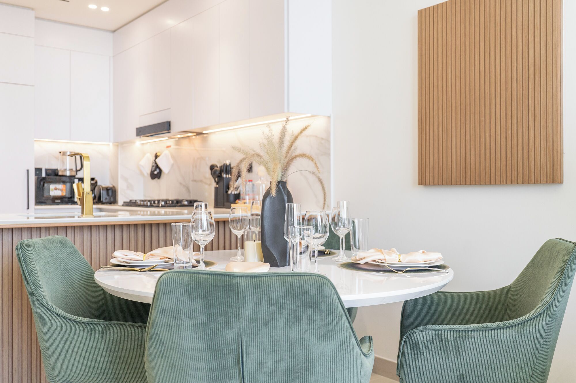 A modern kitchen with a central island, a dining area with green upholstered chairs, and a minimalist decor.