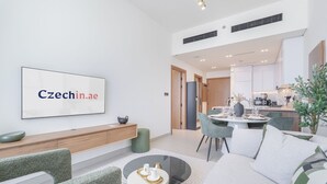 Ein modernes Wohnzimmer mit einem Flachbildfernseher, der 'Czechin.ae' anzeigt, einem Essbereich mit einem runden Tisch und einer Küche im Hintergrund.