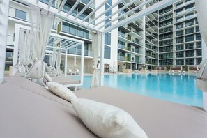 An indoor swimming pool with lounge chairs and a high ceiling with glass panels. - Czechin - Modern 1BHK Binghatti Amber (Dubai)
