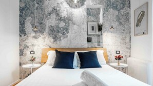A modern hotel room with a large bed, dark blue pillows, a wooden headboard, and a textured wall.