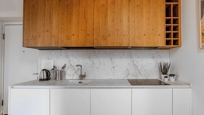 A kitchen with wooden cabinets, a marble countertop, a stainless steel kettle, a sink, and a small potted plant.