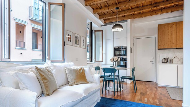 A modern living room with a white sofa, a blue rug, and a wooden ceiling.