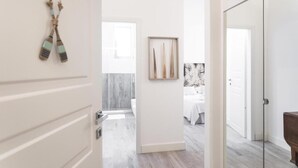 A hallway leading to a bedroom with a bed, a framed artwork, and a wooden door. - Bòmera Rooms (Gallipoli)