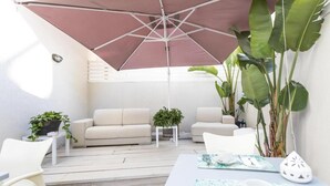 A patio area with a white sofa, two white chairs, a small table, and a large umbrella providing shade. - Bòmera Rooms (Gallipoli)