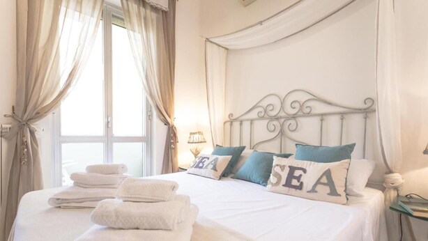 A neatly made bed with folded towels, a decorative headboard, and pillows with the word "SEA" on them. - Bòmera Rooms (Gallipoli)