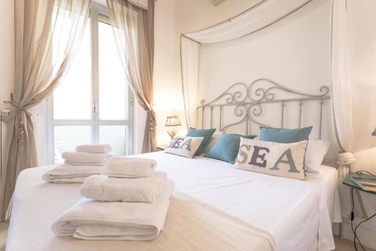 A neatly made bed with folded towels, a decorative headboard, and pillows with the word "SEA" on them.