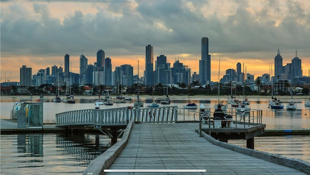 A waterfront cityscape with a marina and a wooden pier leading to a dock.
