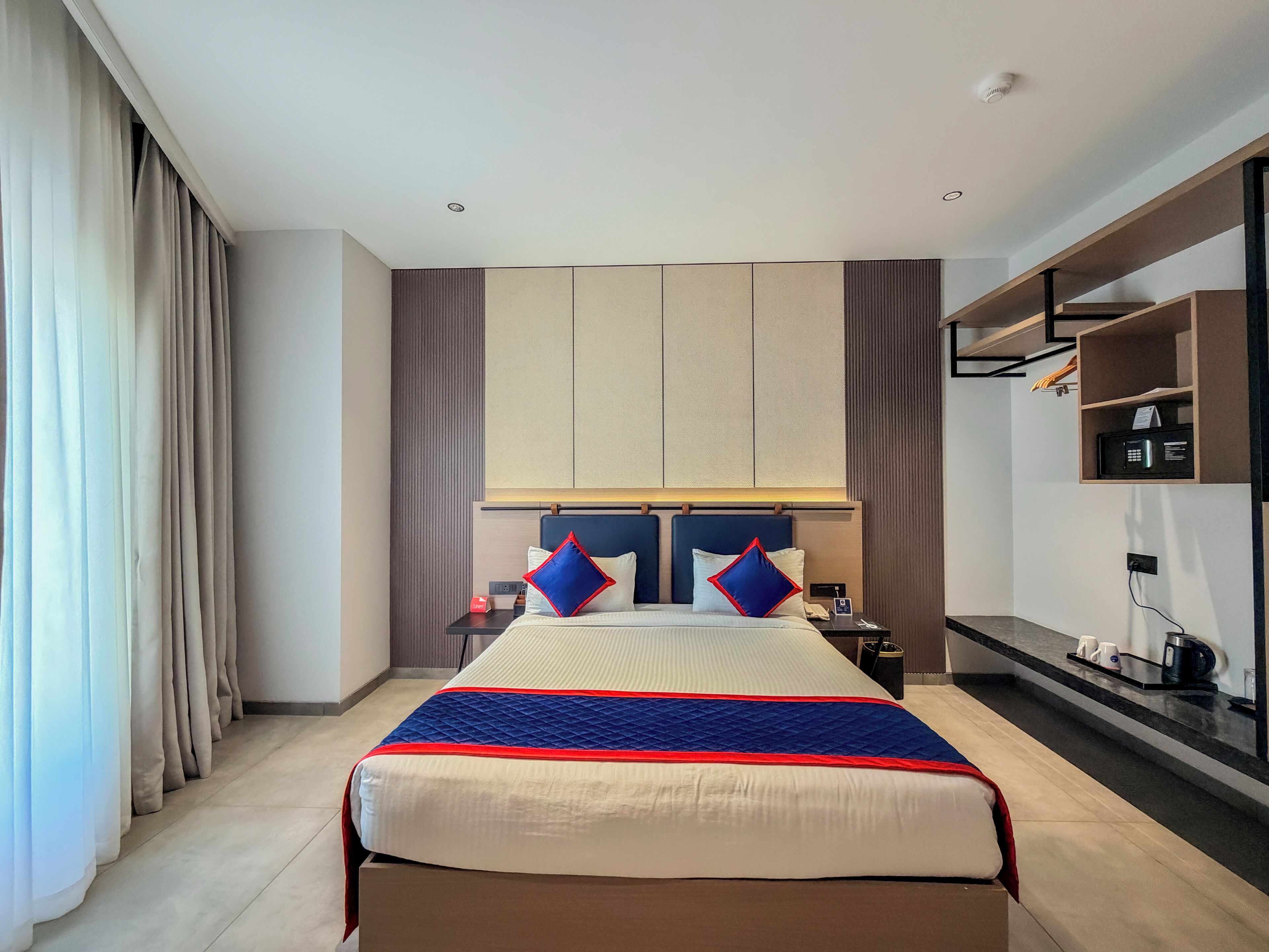 Une chambre d’hôtel avec un grand lit, une table de chevet, une commode, un téléviseur et une étagère intégrée.