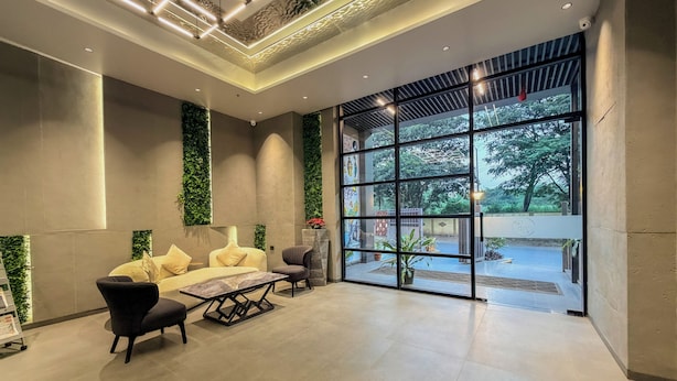 A modern lobby with a sofa set, a coffee table, and a chair. There are large windows with a view of greenery outside. - Zip By Spree Hotels Chinchwad (Pimpri - Chinchwad)
