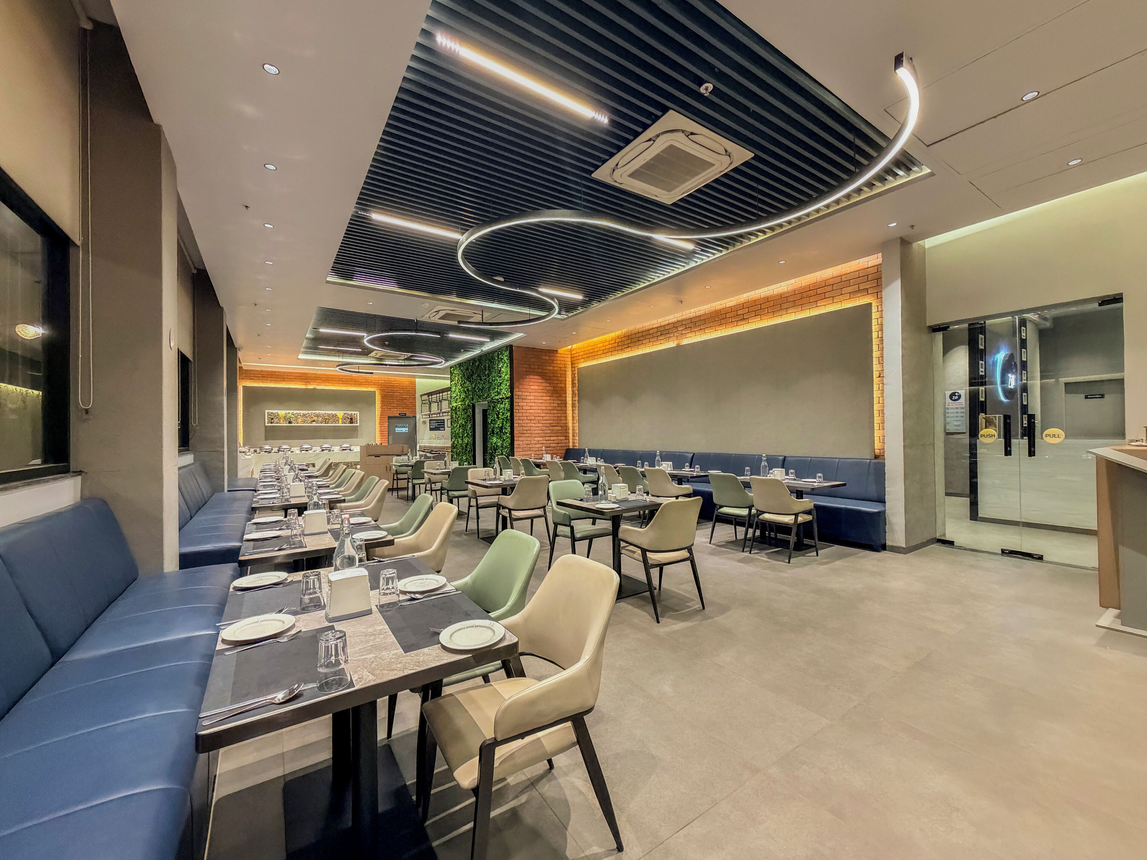 A modern restaurant with a long counter, booths, and a high ceiling with unique lighting.