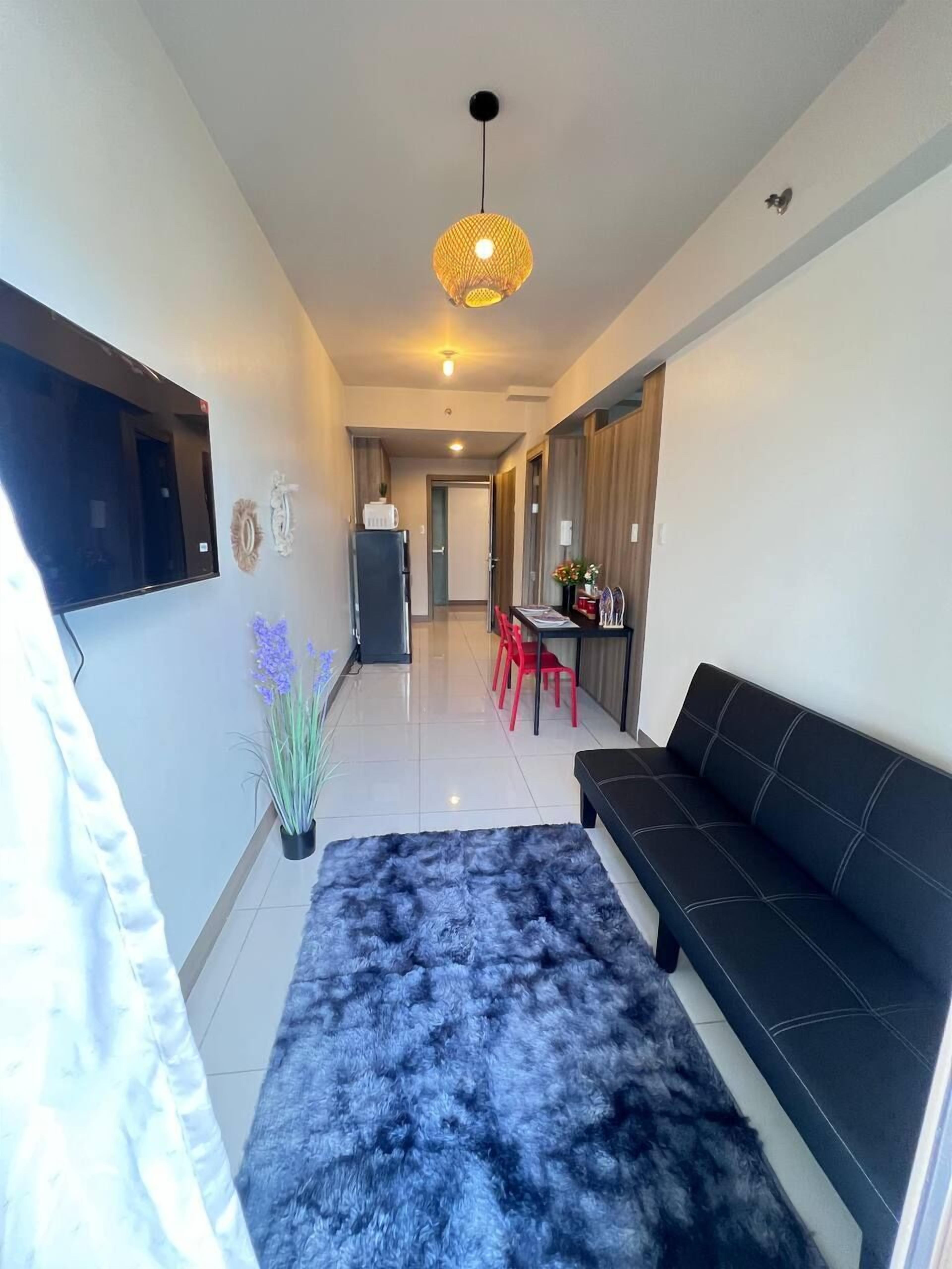 Una sala de estar moderna con un sofá negro, una alfombra peluda azul y una zona de comedor con sillas rojas.