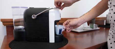 A person operating a coffee machine, with a cup and a glass of water on the counter.
