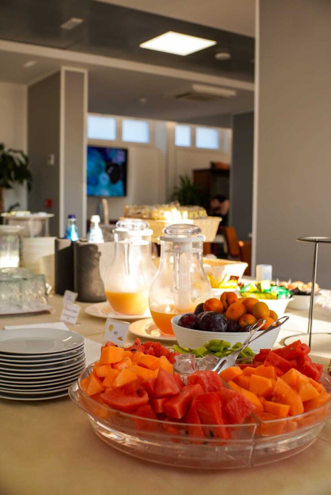 A buffet table with various fruits, a pitcher of orange juice, and a bowl of plums.