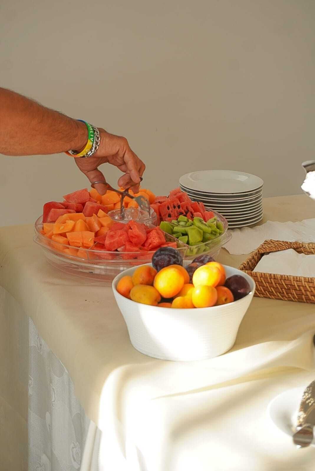 A buffet table with various fruits and a hand reaching for a piece of fruit.