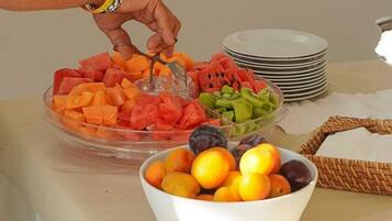 Uma mesa de buffet com diversas frutas e uma mão alcançando uma porção.