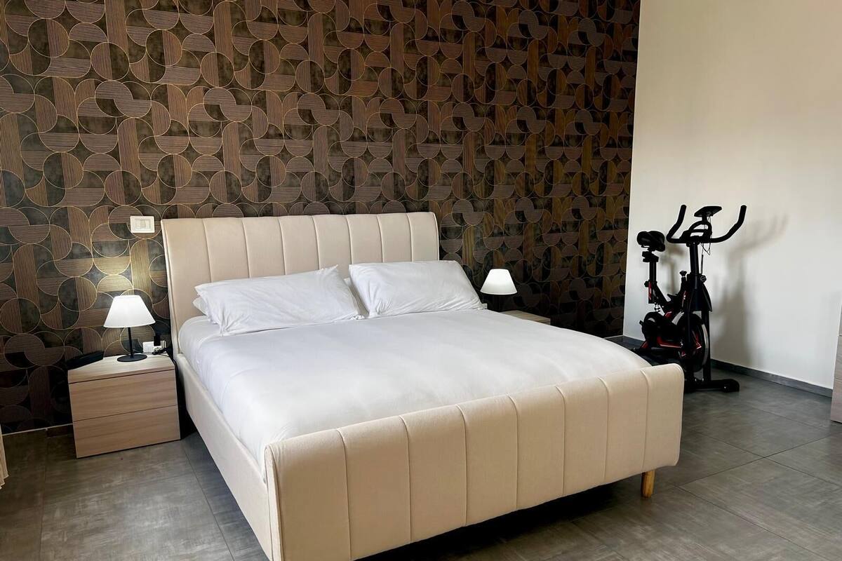 Une chambre à coucher avec un lit, des tables de chevet, une lampe et un vélo d’appartement.