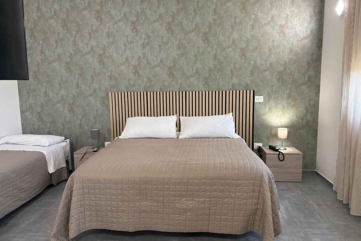 Une chambre d’hôtel avec un grand lit, deux tables de chevet, un téléviseur fixé au mur et un rideau à la fenêtre.