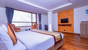 A modern hotel room with a large bed, a flat-screen TV mounted on a wooden wall, a desk, and a chair. - SUMITEL SANDERLING (Darjeeling)