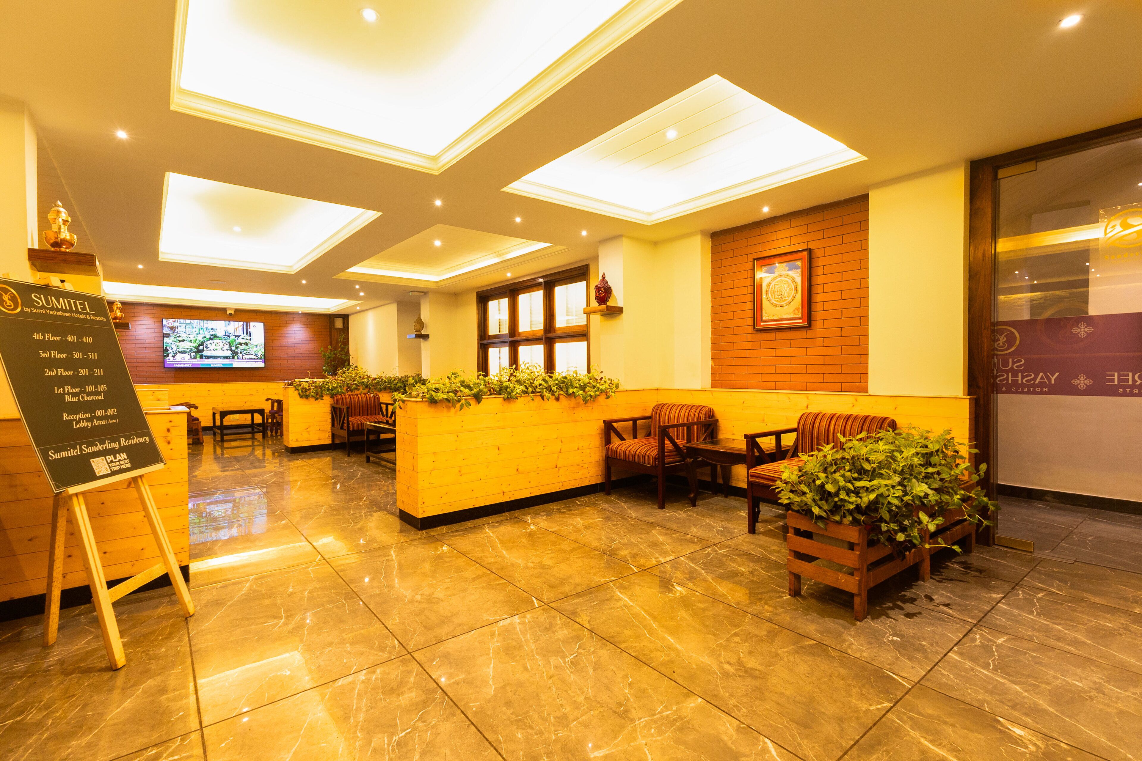 A hotel lobby with a reception desk, seating area, and a TV screen.