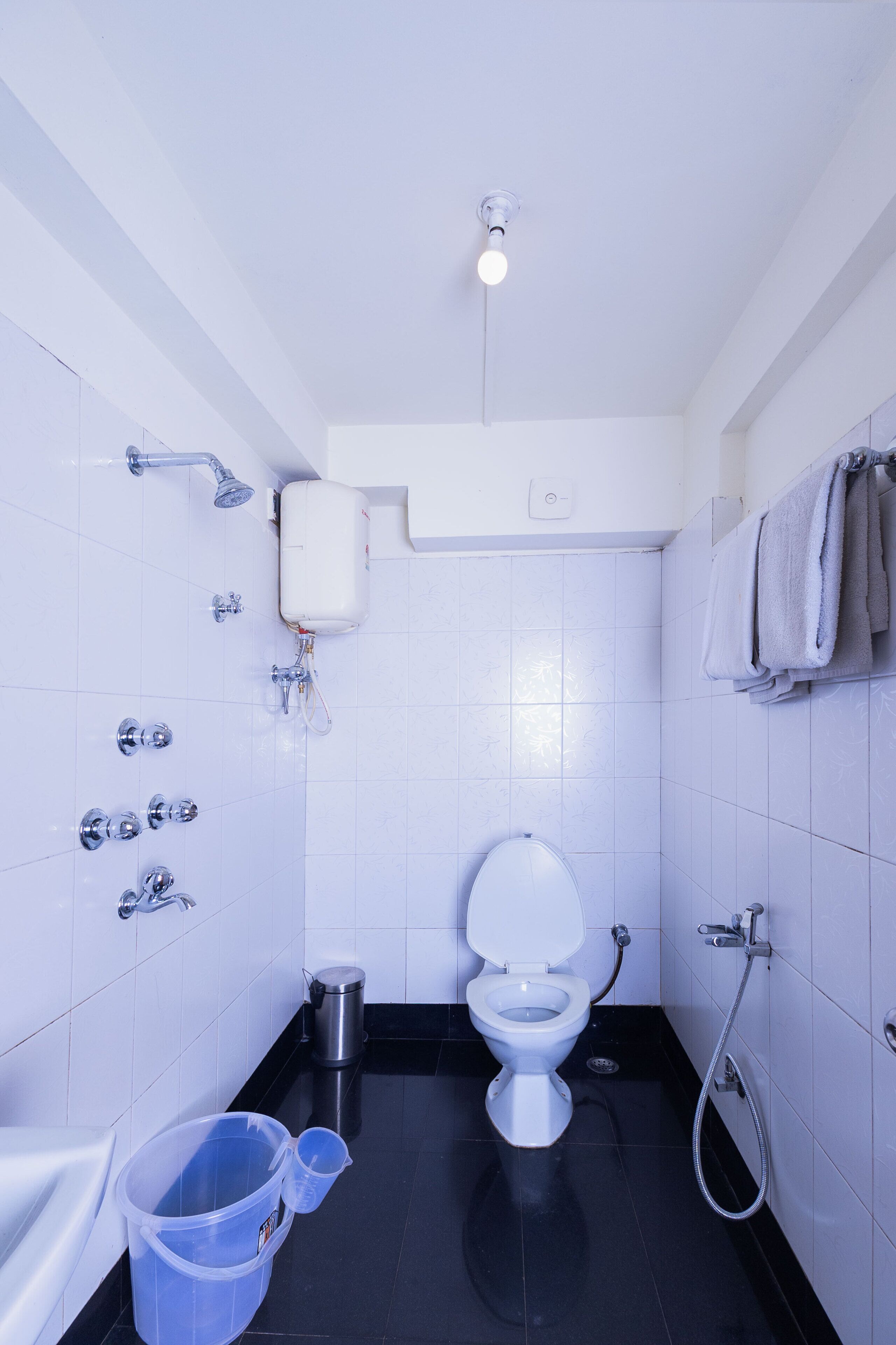 A small, modern bathroom with a toilet, bidet, and shower. There are two buckets and a trash can.