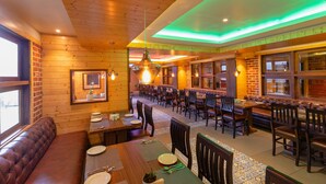 A restaurant with wooden walls, a bar area, and a seating section with tables and chairs. - SUMITEL SANDERLING (Darjeeling)