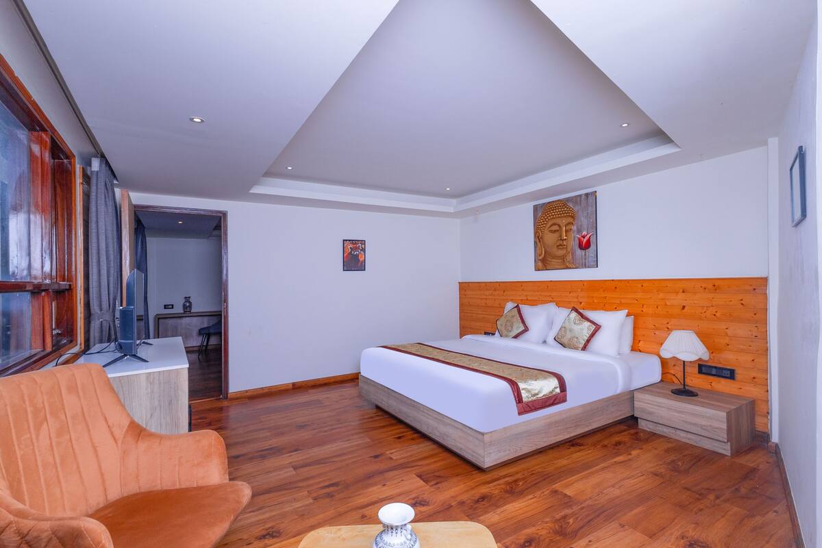 A modern hotel room with a wooden headboard bed, a wooden floor, a desk with a chair, and a large window with curtains.