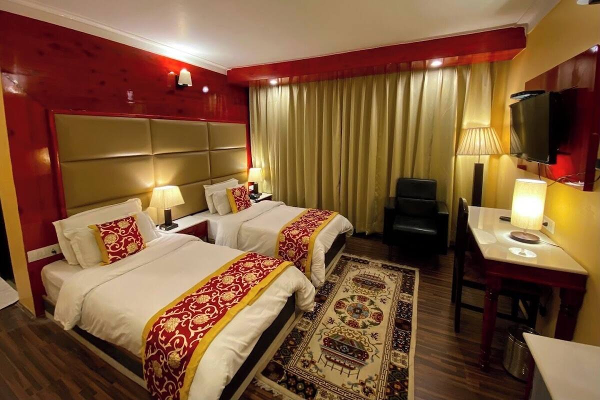 A hotel room with two beds, a desk, a chair, a TV, and a large window with curtains.