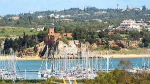 A coastal town with a historic fort, marina with sailboats, and residential buildings on a hillside. - Wake up to marina views in the heart of Praia da Rocha. Steps from the beach, restaurants and bars. Stylish apartment with king-size bed, air conditioning and fully equipped kitchen. Free parking & self check-in. Sleeps up to 5. (Portimão)
