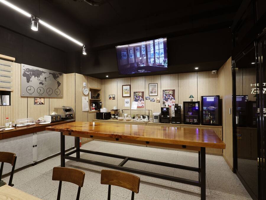 A hotel lobby with a wooden reception desk, seating area, and a television screen displaying a program.