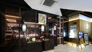 Un interior moderno con fachada de vidrio, paneles de madera y una exposición de cuadros enmarcados.