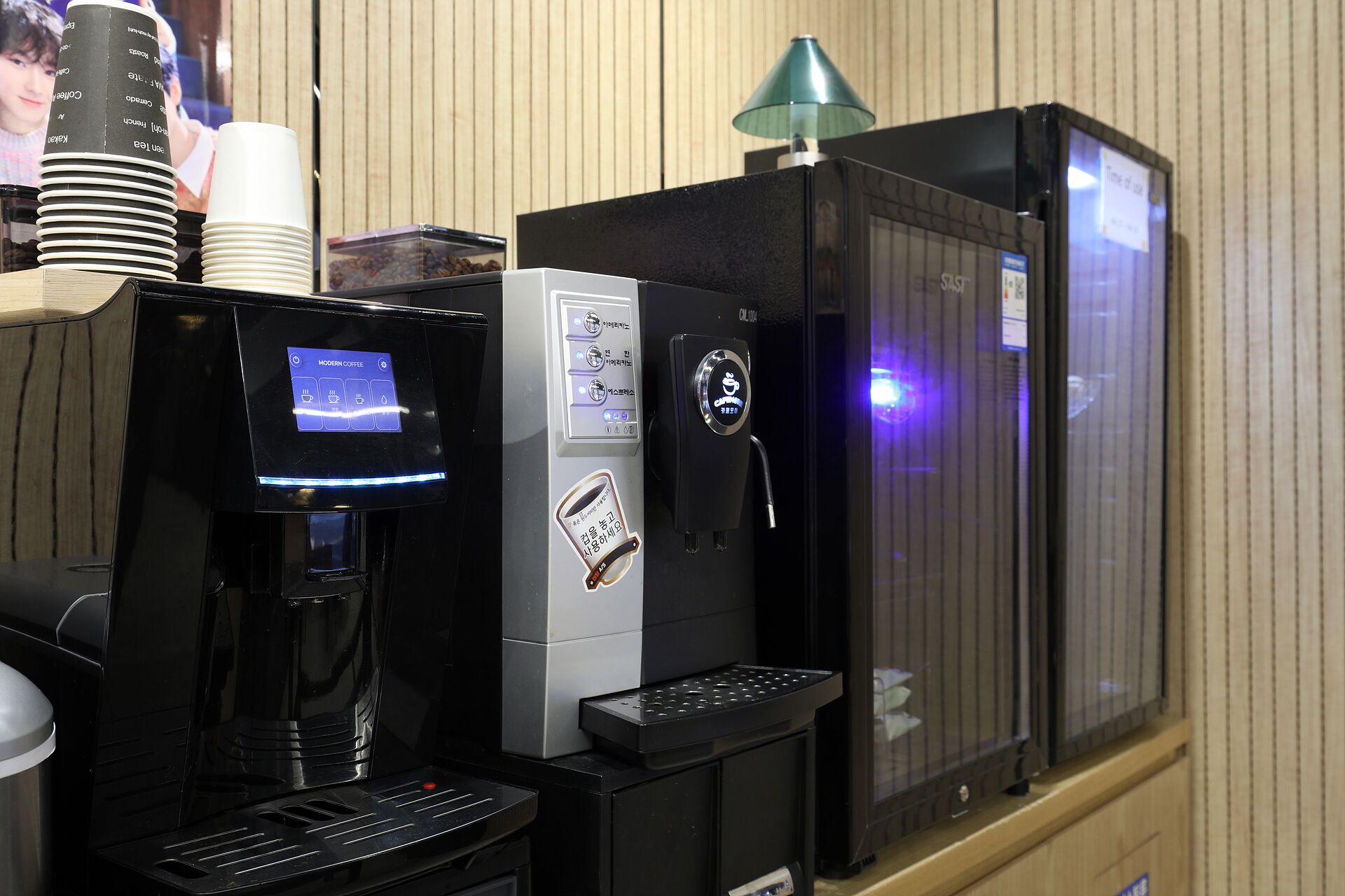 A coffee machine with a digital display, a coffee dispenser, and a stack of disposable cups.