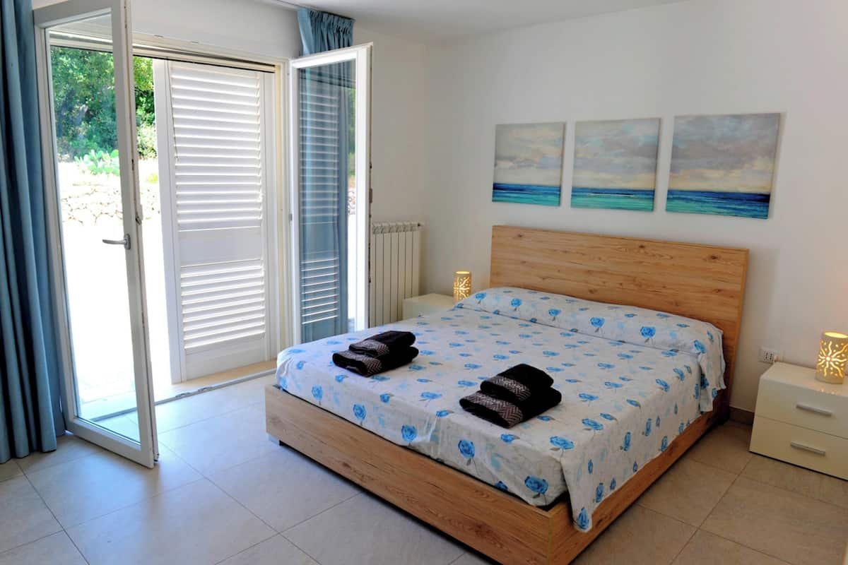 Quarto com cama de madeira, porta de correr de vidro e três quadros na parede.
