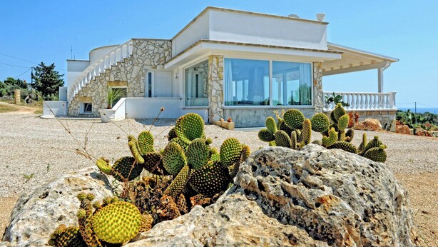 A modern house with a stone facade, large windows, and a balcony overlooking a rocky landscape with cacti. - Complesso Villa Vanissia (Castrignano del Capo)